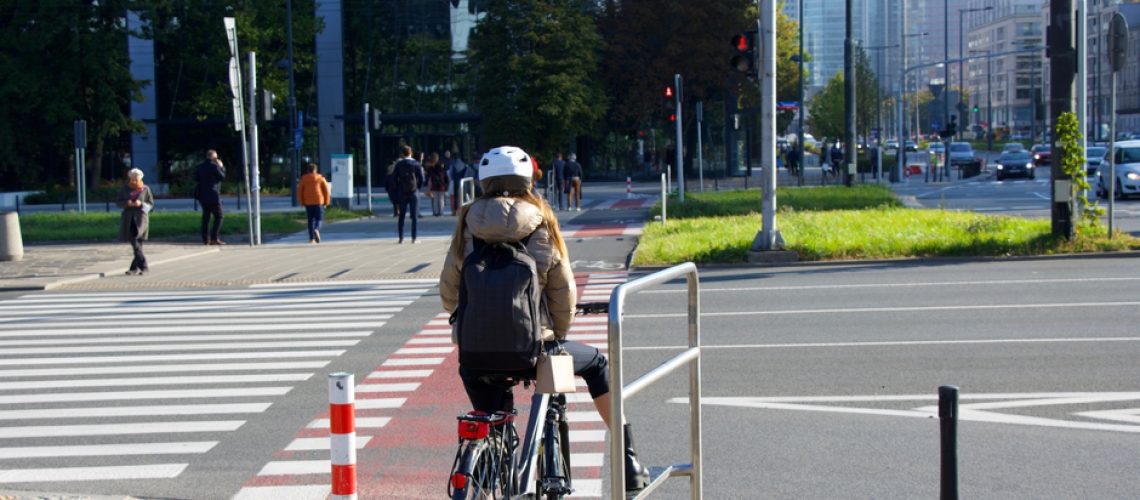 Cyclist at zebra crossing wait for the traffic lights change. Skyscrapers and a modern city in the background. Modern eco transport in the city.